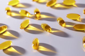 Shiny yellow gel capsules casting shadows on white surface