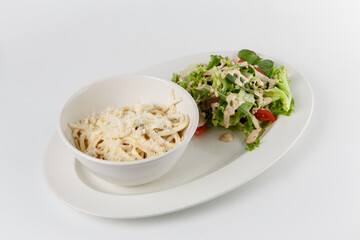 Creamy pasta with parmesan and fresh salad on white plate
