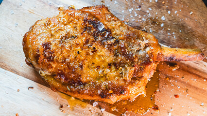 A perfectly grilled, juicy pork chop with the bone-in, seasoned with fresh herbs and garnished with flaky Maldon salt. This succulent cutlet is a hearty and delicious meal, captured steaming hot.