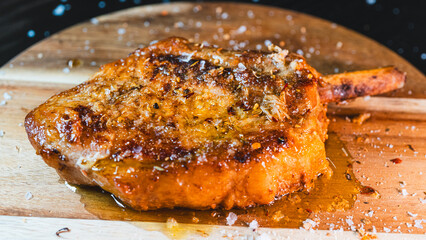 A perfectly grilled, juicy pork chop with the bone-in, seasoned with fresh herbs and garnished with flaky Maldon salt. This succulent cutlet is a hearty and delicious meal, captured steaming hot.