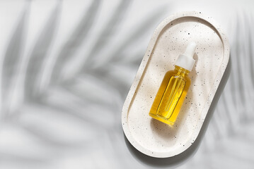 A beauty serum in a dropper bottle flat lay on a ceramic tray in sunlight and shadows from palm leaves. Top view.