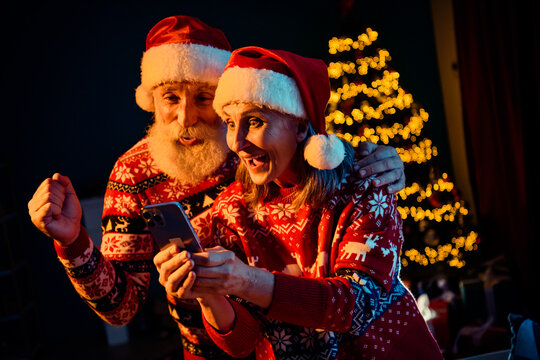 Joyful retired couple in festive sweaters and Santa hats share a happy moment at home as they video chat by a glowing Christmas tree a warm holiday scene filled with magic and love