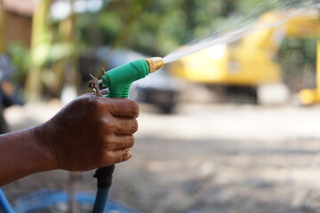 Dark hand with green hose spraying water machinery in background. Suitable for industrial,...