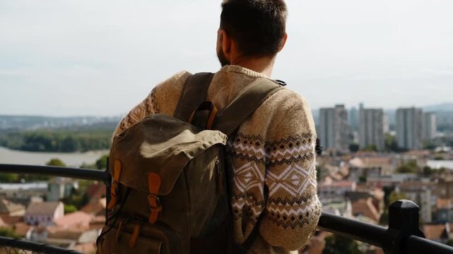 A man with a backpack stands on Gardos Tower in Zemun, spreading his arms and enjoying the city view of Belgrade. Solo travel concept