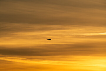 Silhouette of a passenger airplane flying through a vast, beautiful golden sky at sunset, symbolizing travel and new journeys.