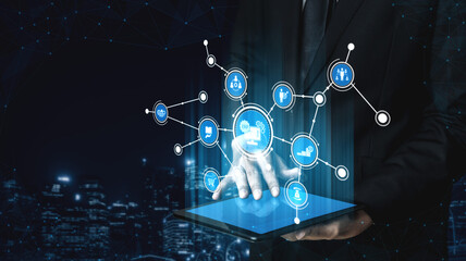 A businessman interacts with a tablet showcasing holographic icons, representing modern technology and digital innovation in a dynamic urban environment. Tessel