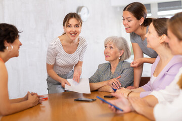 during meeting,young employee stands at table holding documents in hands and argues her position. Using printed report, young student explains to colleagues how to achieve goal