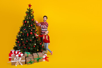 Dad and daughter decorating a Christmas tree with colorful ornaments on a bright yellow background, embracing holiday spirit