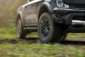Off-road black pickup truck with mud tires driving on grassy trail outdoors with motion effect