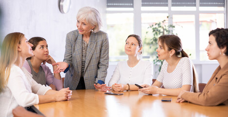 Women of different ages in casual clothes communicate at table in office..