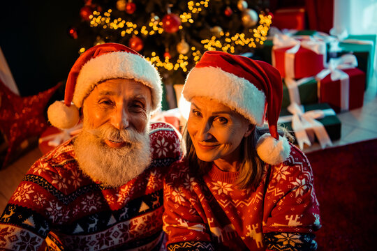 Warm christmas couple in santa hats smiling together by decorated tree with gifts in cozy home scene to evoke holiday joy - Powered by Adobe