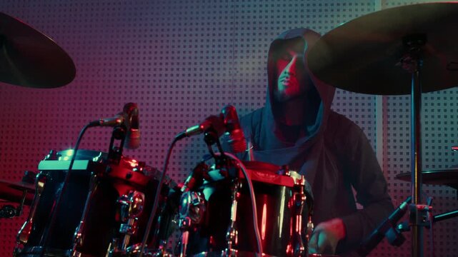 A drummer passionately performs on a drum set, illuminated by vibrant red and blue lighting, showcasing rhythm and energy in a modern studio setting