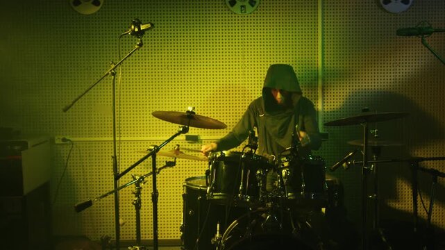 A drummer passionately performs on a drum set, illuminated by striking green lighting, showcasing rhythm and energy in a modern recording studio