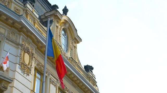Romanian flag waving proudly on the side of a government building, showcasing national identity and patriotism against a backdrop of blue sky and vibrant colors