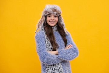 Beautiful teen girl in a winter hat and a warm sweater. A child on a yellow isolated background. Happy face, positive and smiling emotions of teenager girl.