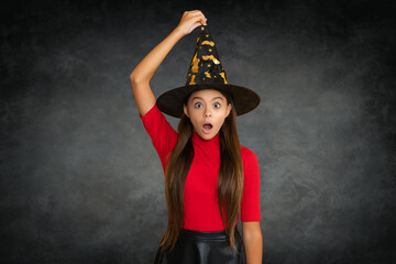 Funny kid girl in Halloween hat on black. Halloween witch teen girl. Little girl witch. Kid witch celebrates Halloween. Portrait of an Halloween child teen girl.