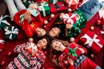 Happy friends exchange gifts lying on festive rug surrounded by decorations and presents during a cozy Christmas celebration