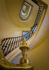 Interior view of a classic oval staircase surrounded by yellow-painted walls and detailed cast iron railings