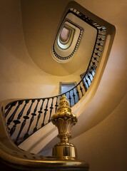 Interior view of a classic oval staircase surrounded by yellow-painted walls and detailed cast iron railings