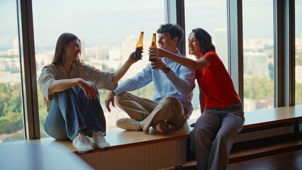 Happy friends sipping beer from bottles panoramic window. People toasting drinks