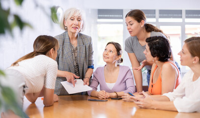 Women of different ages in casual clothes discussing documents at table in office