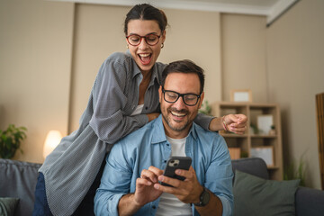 Smiling couple have fun while use mobile phone together at home