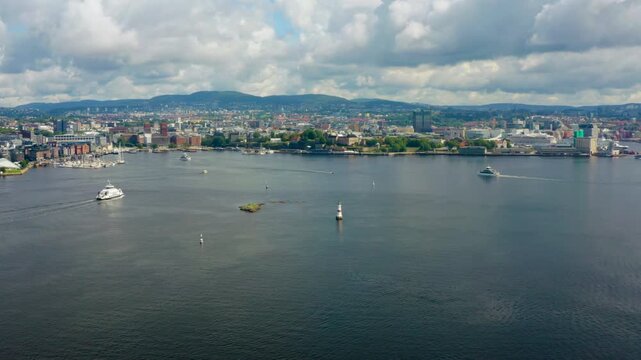 Smooth aerial zoom-in of a ferries and boats navigating Oslofjord, with Oslo coastline and nearby islands in the frame. Summer maritime movement and scenic urban nature contrast in Norway