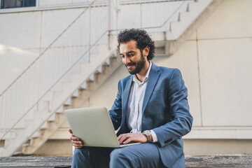 Smiling businessman working on laptop outdoors in urban setting