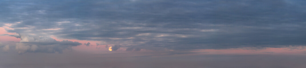 Full moon rising through dark clouds on pink clear sky.