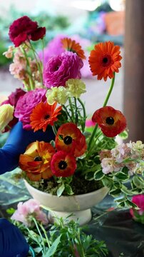 Florist inserts orange ranunculus into a colorful wedding ekibana in a vase. wedding flower arrangement