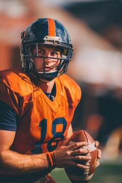 Quarterback in orange uniform holding ball on field looking focused during active college football practice session outdoors