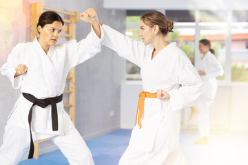 Obraz premium Concentrated young Asian woman in kimono and black belt honing punching techniques during training sparring with female opponent at karate workout..