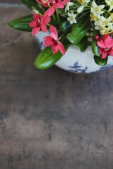 Vaso de cer&acirc;mica branco com flores do campo brancas e rosadas sobre fundo marrom r&uacute;stico.
White ceramic vase with white and pink wildflowers on a rustic brown background