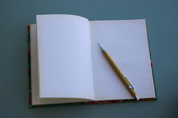 Caderno aberto sobre base neutra, com lapiseira amarela sobre a folha branca.
Open notebook on a neutral background, with a yellow mechanical pencil on the white page.