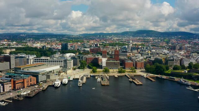 Drone zoom-out shot revealing Oslo downtown skyline with City Hall and iconic waterfront landmarks. Captures Scandinavian urban density, architectural contrast, and scenic Norwegian harbor setting.