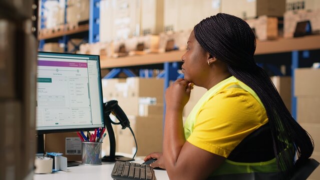 Warehouse employee using package tracking software on computer monitor, managing express delivery and using awb tracking info to update real time parcel status. Distribution hub. Camera B.