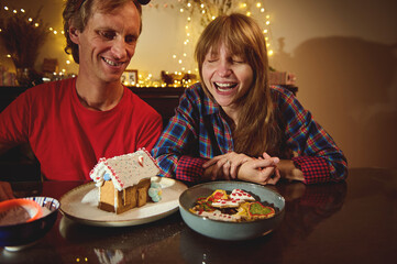 Joyful Couple At Christmas Table With Gingerbread House And Cookies In A Cozy Festive Kitchen