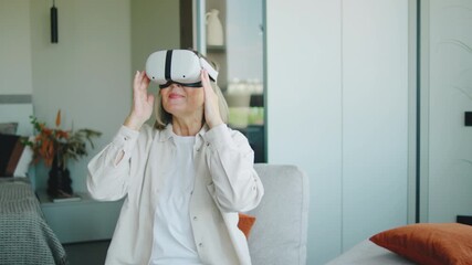 Senior woman engages with virtual reality technology in a modern living room, experiencing new adventures and activities at home - Powered by Adobe