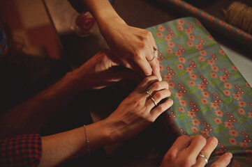 Obraz premium Pair Of Hands Sewing Fabric With Floral Pattern On Table, Crafting Moment Of Shared Sewing, Friendship And Creative Work