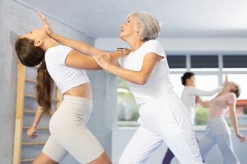 Concentrated senior woman practicing effective self-defense techniques in sparring with young...
