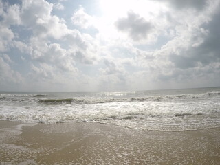 Bright Cloudy Sky Over Ocean Waves and Sandy Beach Shoreline