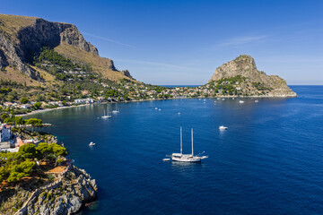 Fototapeta premium Sant Elia bay beach in Porticello town, Santa Flavia, Sicily, Italy, aerial drone view of Sicilian turquoise waters, rocky cliffs, colorful houses, and Mediterranean coastline panorama in Bagheria