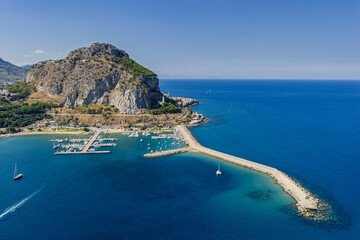 Aerial drone view of Scalette Beach in Cefalu, Sicily, Italy. the Tyrrhenian Sea, Capo Cefalu Lighthouse, rocky cliffs, Cefalu Harbor, and medieval castle ruins with scenic coastline panorama