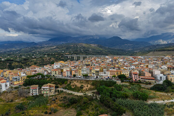 Naklejka premium Aerial drone view of Campofelice di Roccella, a historic Sicilian village in Palermo,Sicily, Italy, featuring traditional stone houses, the Madonie Mountains, and the iconic highway viaduct