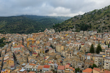 Fototapeta premium Aerial drone view of Collesano Sicilian mountain town at sunset with Basilica San Pietro church and historic stone streets in the Madonie Mountains, Sicily, Italy. Old mountain town in Sicily