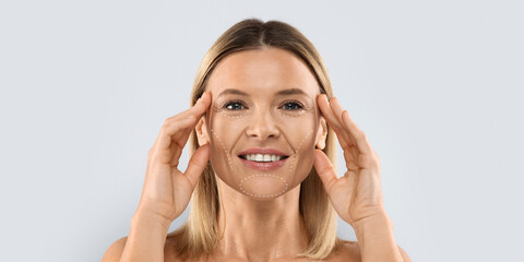 Obraz premium A woman is smiling while holding her face with both hands. She appears to be engaged in a facial care routine.