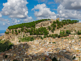 Naklejka premium Aerial drone view of Caltavuturo, a historic Sicilian mountain town in Palermo, Italy, featuring its medieval castle, rugged surrounding cliffs, and scenic landscapes of the Madonie Mountains
