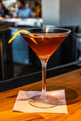 A classic Manhattan cocktail, garnished with a lemon twist, rests elegantly on a bar counter, showcasing its rich amber hue in a sophisticated martini glass, evoking a timeless drinking experience.