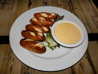 Warm, golden pretzel sticks with sea salt, served alongside a creamy cheese dip and a fresh lettuce garnish, perfect for a savory snack or appetizer.