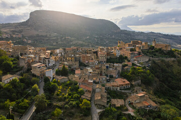 Fototapeta premium Aerial drone view of Collesano Sicilian mountain town at sunset with Basilica San Pietro church and historic stone streets in the Madonie Mountains, Sicily, Italy. Old mountain town in Sicily